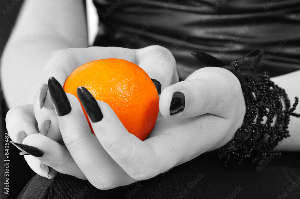 Naklejka premium Colored mandarine in black-white hands of a gothic girl
