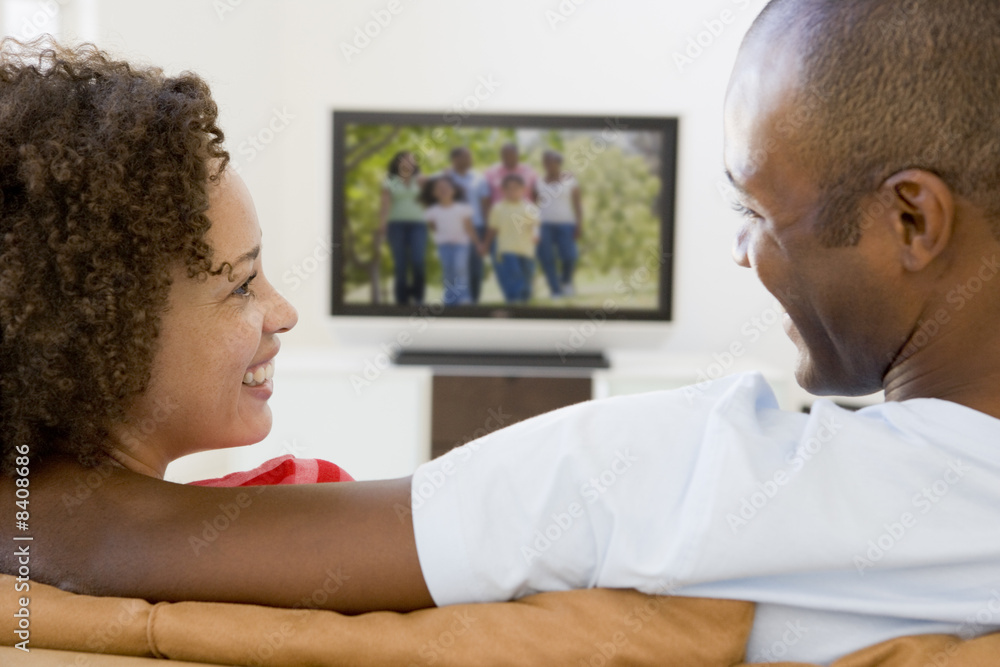 Couple in living room watching television smiling Couple in living room watching television smiling