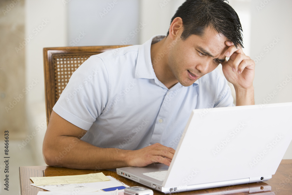 Man in dining room using laptop and frowning Man in dining room using laptop and frowning