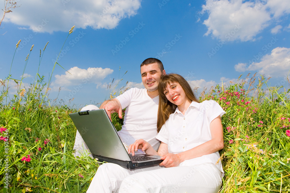 Young couple sitting on the grass field with a laptop. Young couple sitting on the grass field with a laptop.