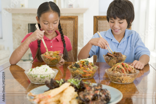 Two young children eating chinese food in dining room