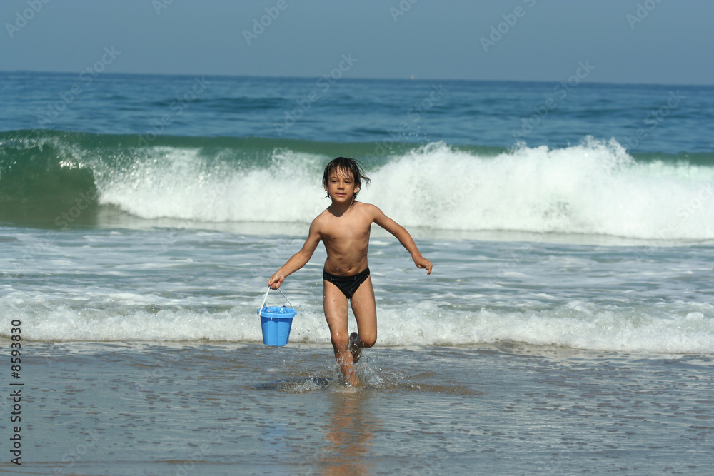 petit garçon entrain de courir avec un seau sur la plage petit garçon entrain de courir avec un seau sur la plage