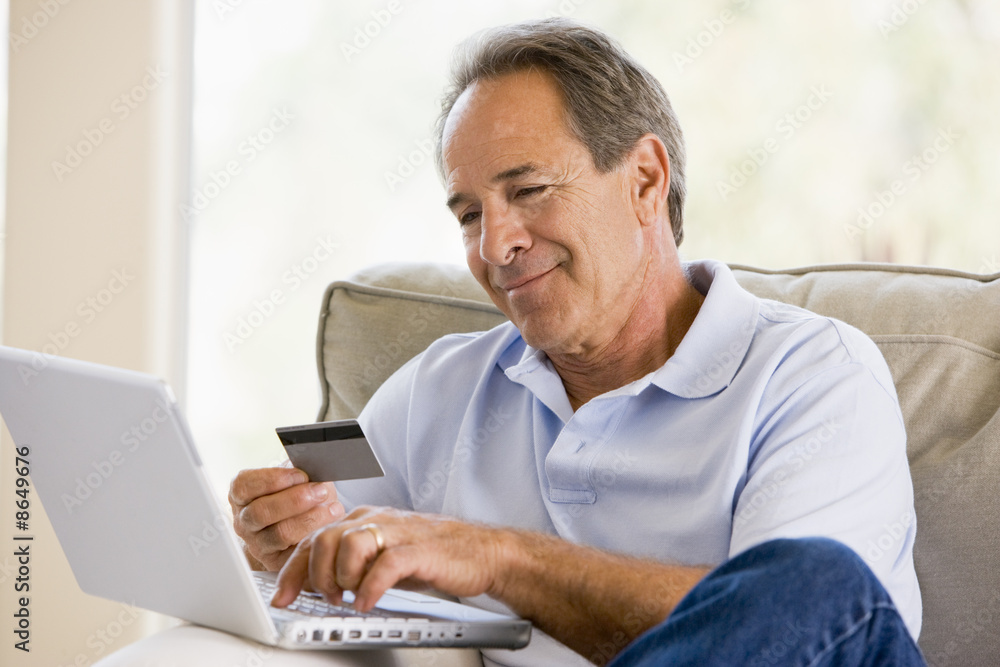 Man in living room with laptop and credit card smiling Man in living room with laptop and credit card smiling