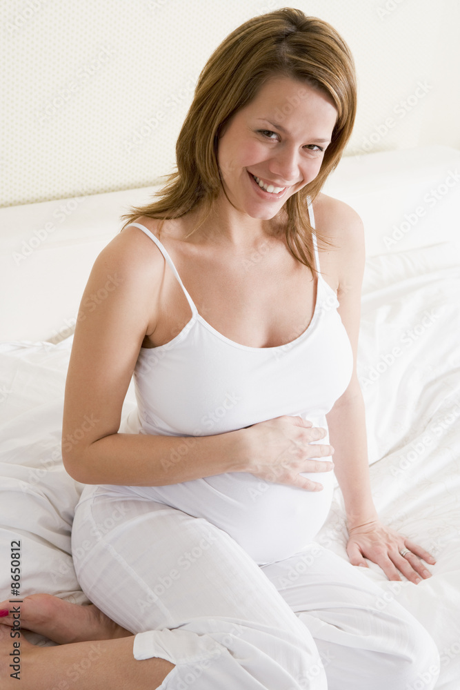 Pregnant woman sitting in bed smiling Pregnant woman sitting in bed smiling