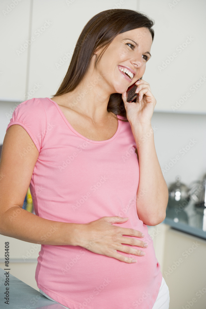 Pregnant woman in kitchen talking on cellular phone and smiling Pregnant woman in kitchen talking on cellular phone and smiling