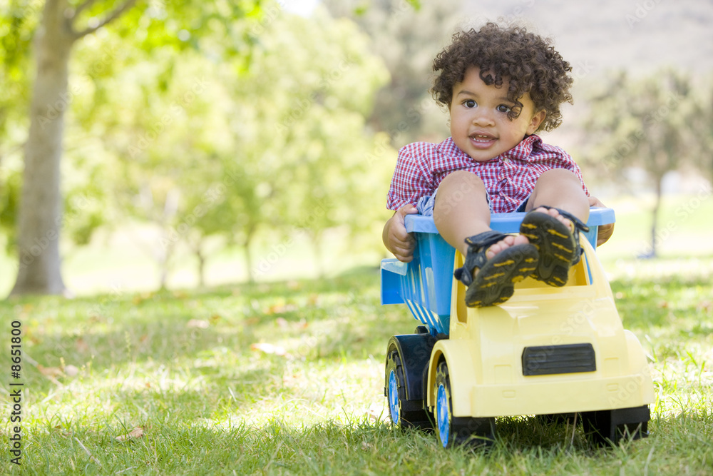 Young boy outdoors playing on toy dump truck smiling Young boy outdoors playing on toy dump truck smiling