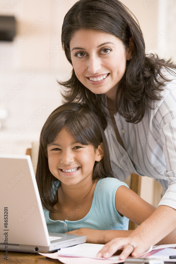 Woman and young girl in kitchen with laptop and paperwork smilin