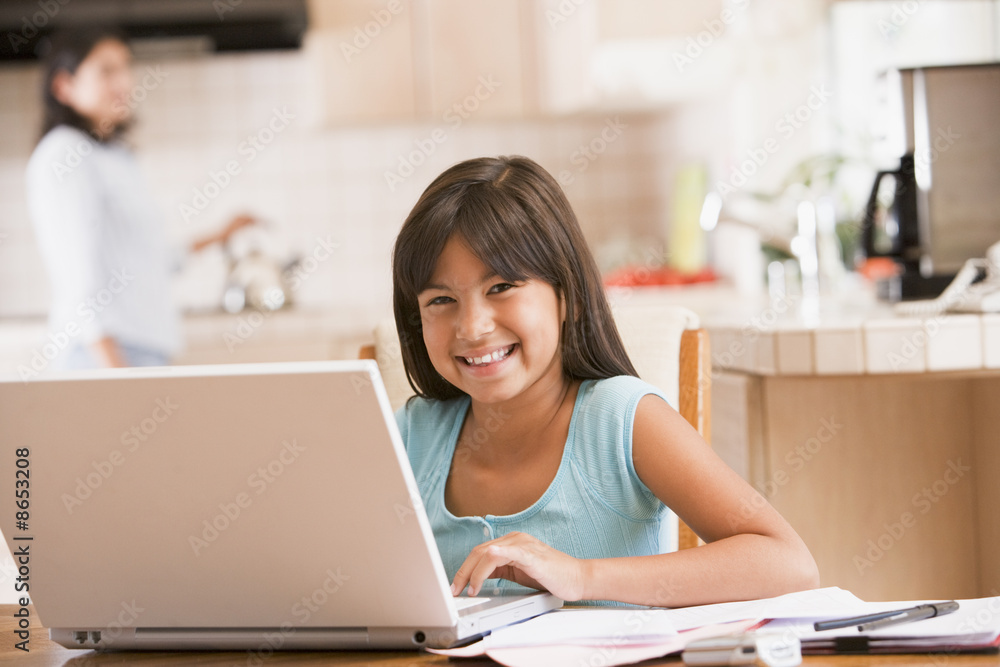 Young girl in kitchen with laptop and paperwork smiling with wom Young girl in kitchen with laptop and paperwork smiling with wom