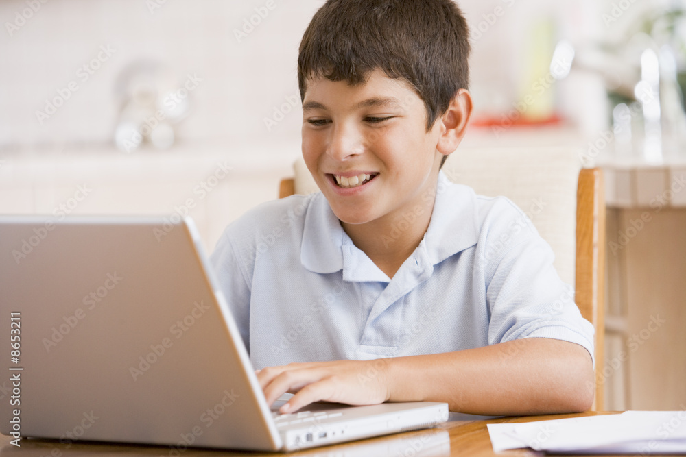 Young boy in kitchen with laptop and paperwork smiling Young boy in kitchen with laptop and paperwork smiling