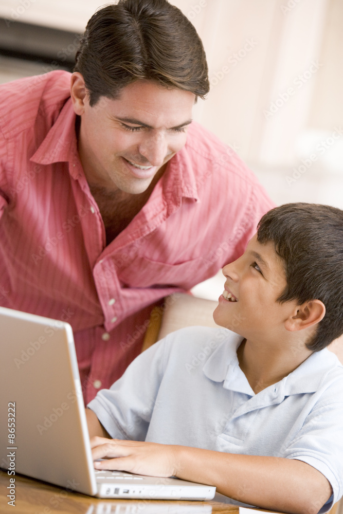 Obraz premium Man helping young boy in kitchen with laptop smiling