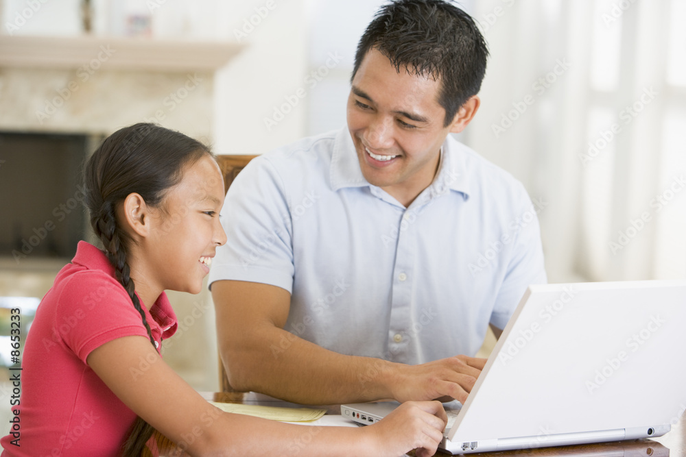Man and young girl with laptop in dining room smiling Man and young girl with laptop in dining room smiling