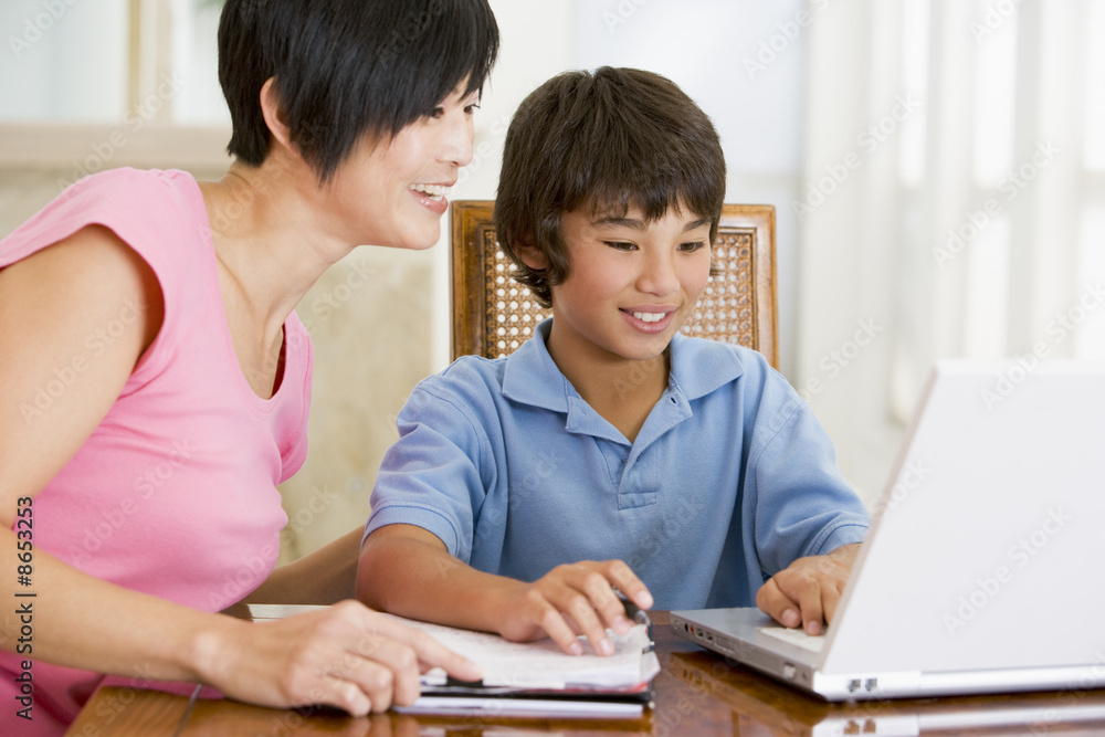 Woman helping young boy with laptop do homework in dining room s Woman helping young boy with laptop do homework in dining room s