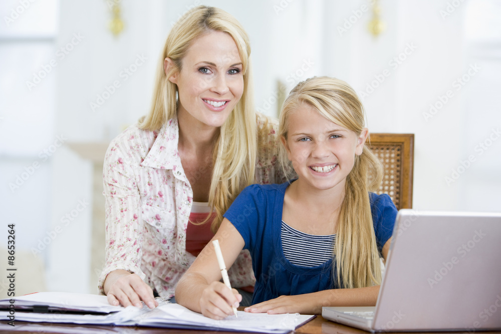 Woman helping young girl with laptop do homework in dining room