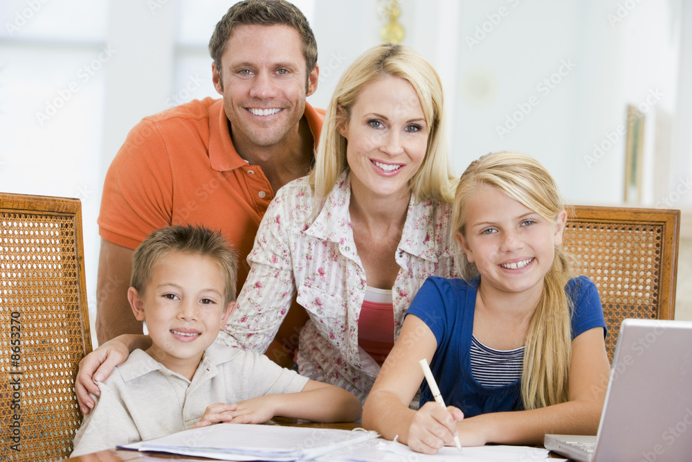 Couple helping two young children with laptop do homework in din Couple helping two young children with laptop do homework in din