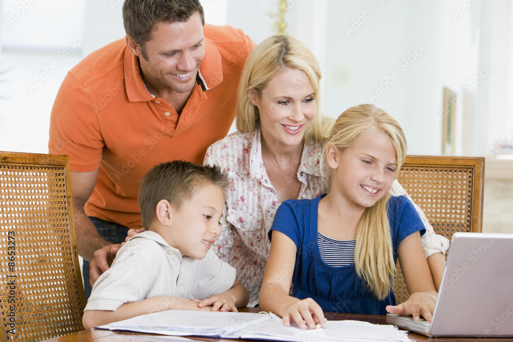 Couple helping two young children with laptop do homework in din Couple helping two young children with laptop do homework in din