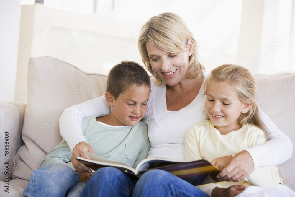 Woman and two children sitting in living room reading book and s Woman and two children sitting in living room reading book and s