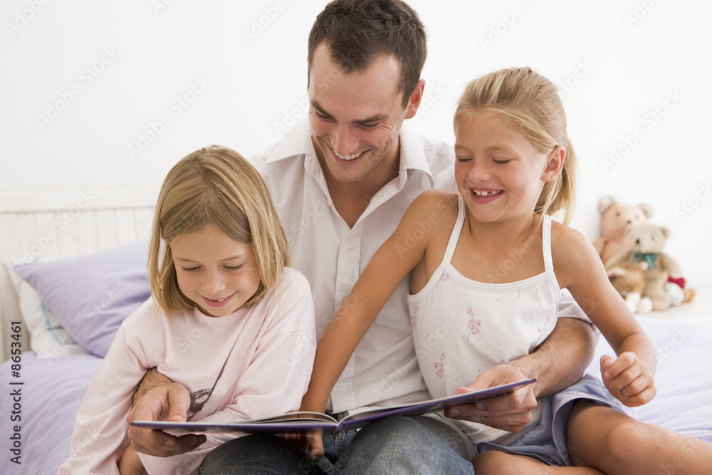 Man in bedroom with two young girls reading book and smiling