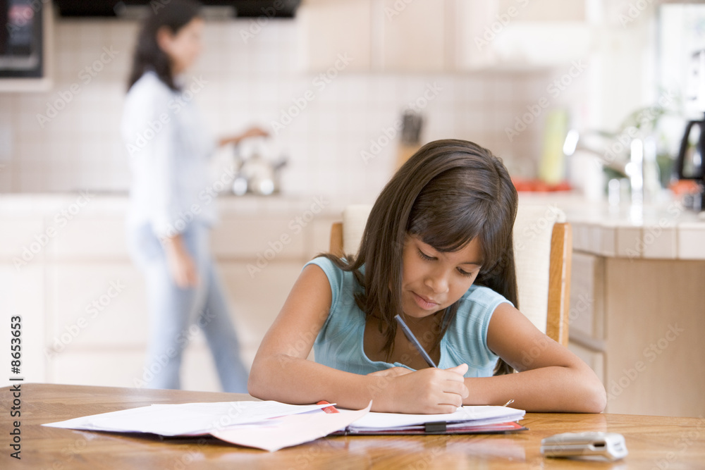 Young girl in kitchen doing homework with woman in background Young girl in kitchen doing homework with woman in background