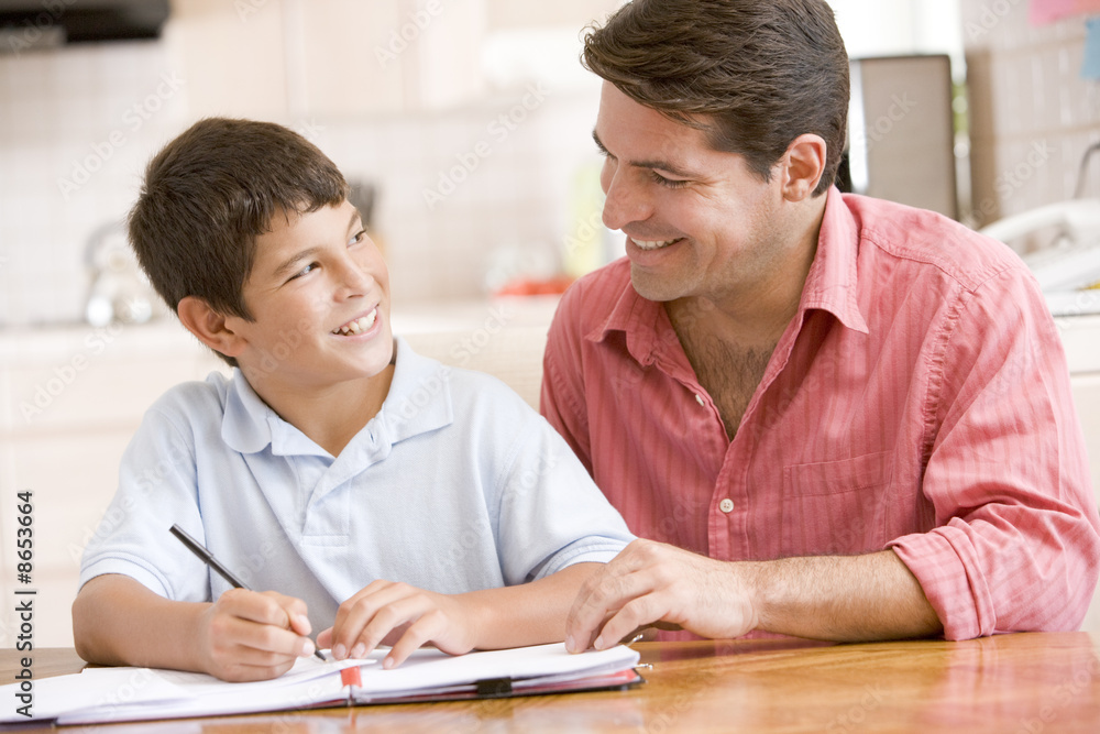 Man helping young boy in kitchen doing homework and smiling Man helping young boy in kitchen doing homework and smiling