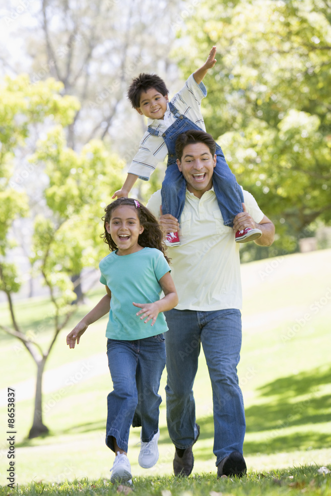 Man with two young children running outdoors smiling Man with two young children running outdoors smiling