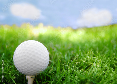 Golf ball closeup, on the tee, with grass and sky