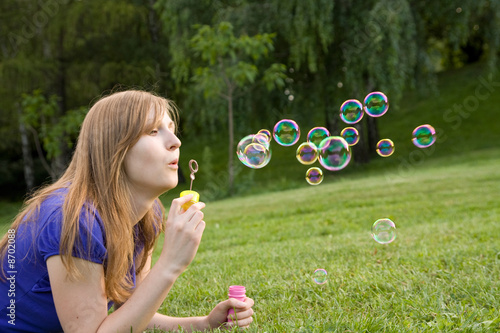 beautiful girl makes soap bubble on a grass