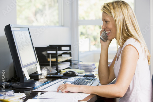 Woman in home office with computer using telephone smiling photo