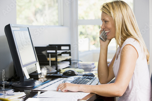 Billede på lærred Woman in home office with computer using telephone smiling