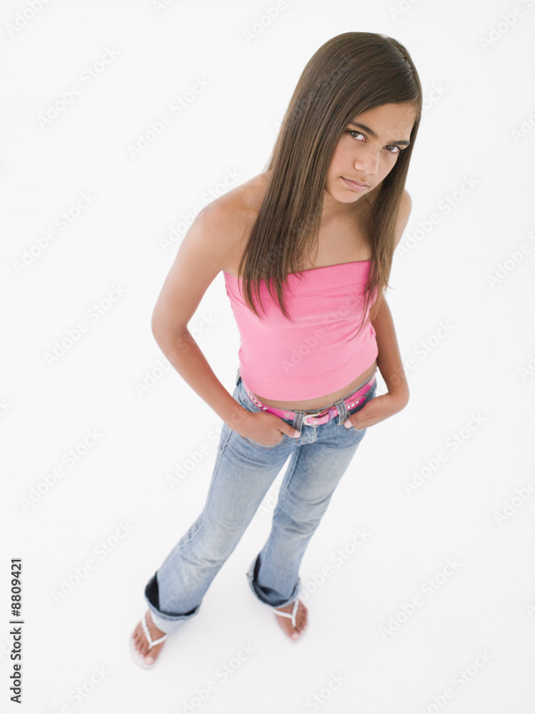 Young girl standing with hands in pockets frowning