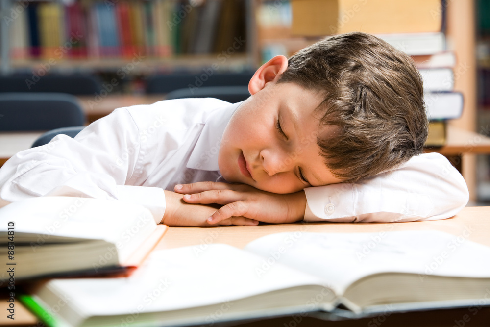 Image of young boy sleeping near books in the library Image of young boy sleeping near books in the library