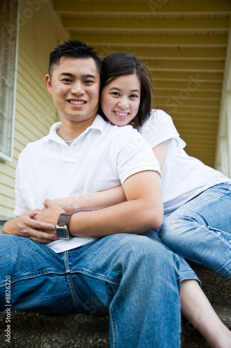 An asian couple sitting on the porch in front of their house