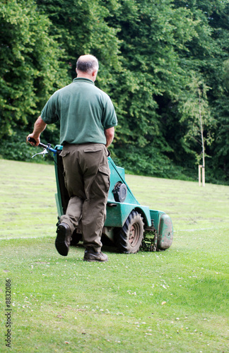 A photograph of a man mowing the grass in a public park