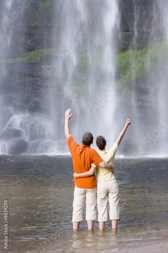 Paar mit erhobenen Armen vor tropischem Wasserfall