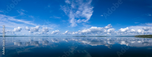Blue bright summer sky with white clouds reflecting in lake