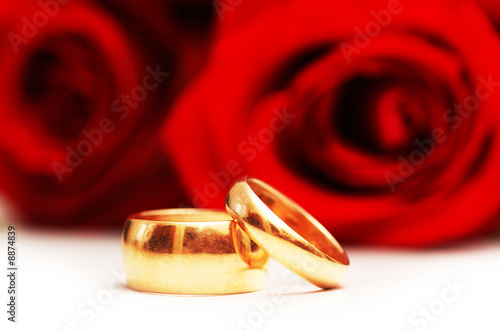 Two wedding rings and red roses isolated on white