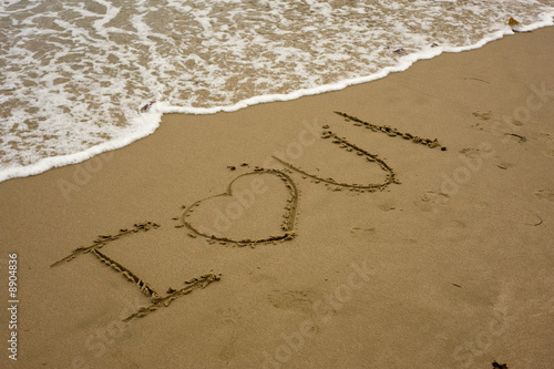 The words "I Love You" written on a sandy beach with water