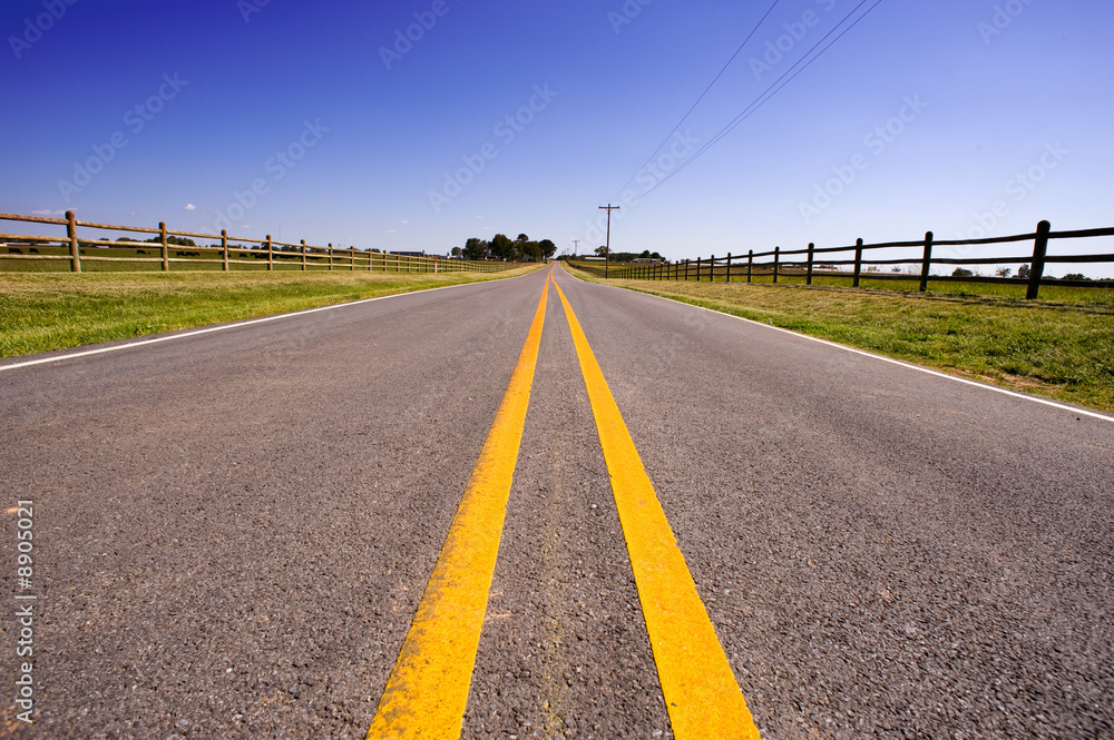 Fototapeta premium A long road bordered by farm fences and telephone wire