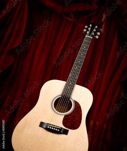 A classic dreadnought guitar on a red curtain background