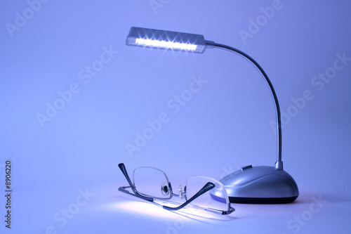 Table lamp and modern spectacles lying on blue background photo