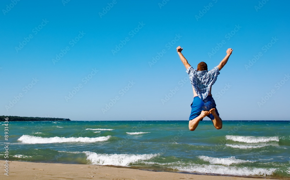 Happy man jumping over sea. Sand beach and blue water.