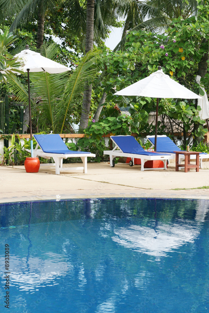Obraz premium Deck chairs and umbrellas next to a swimming pool.