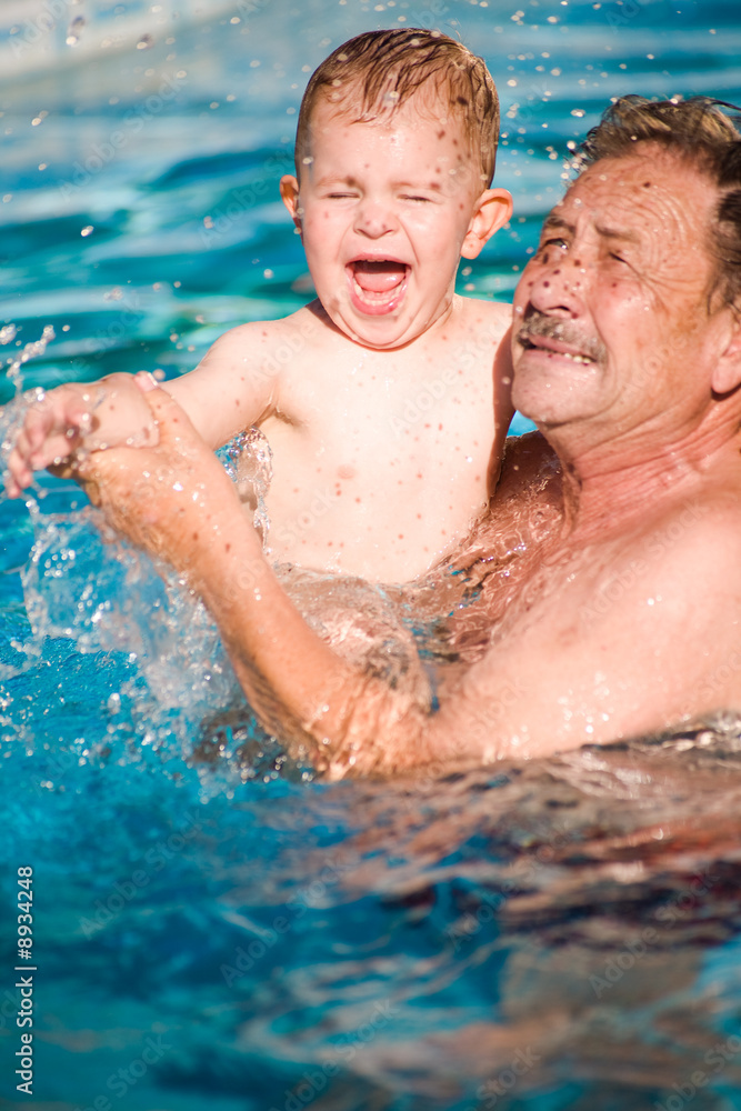 Grandfather and grandson playing together in pool, summer
