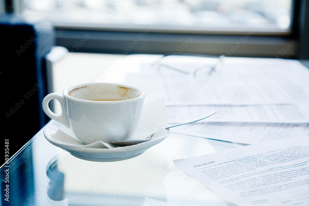 A cup of coffee, eyeglasses and papers lying on the table A cup of coffee, eyeglasses and papers lying on the table