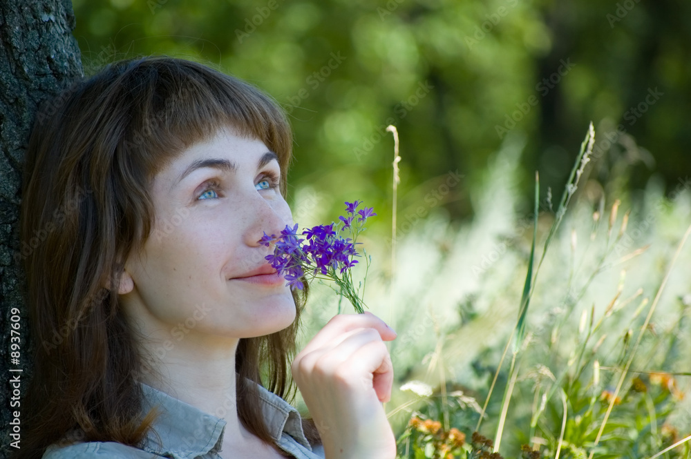Girl sits on a grass under the tree and smells a flowers Girl sits on a grass under the tree and smells a flowers