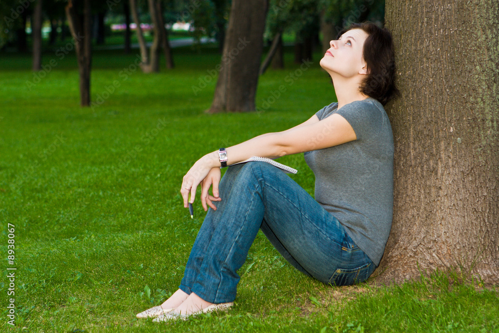 Girl sits under a tree with a thoughtful kind Girl sits under a tree with a thoughtful kind