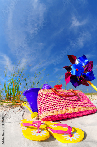 Pretty array of beach accessories on sand dune under blue sky