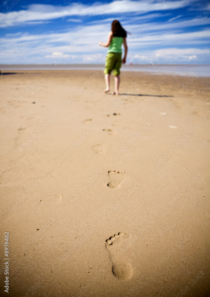 Young girl walking on the beach leaving footprints in the sand