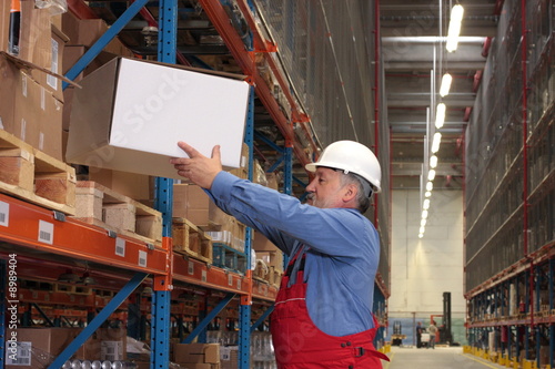 senior worker in uniform putting box on shelf in warehouse