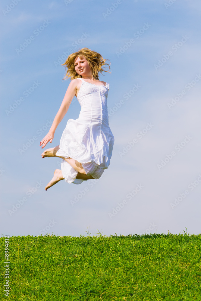 Girl jumps on a green grass on a background of the blue sky Girl jumps on a green grass on a background of the blue sky