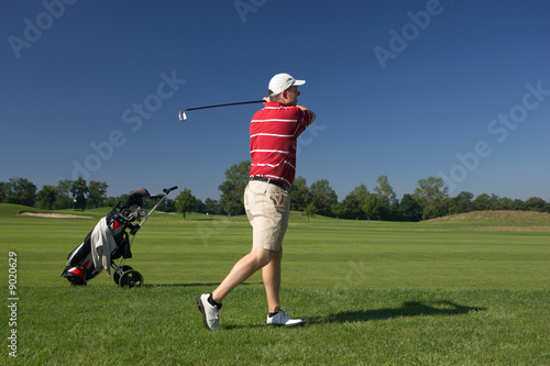 caucasian golfplayer with golfcart teeing off on grass